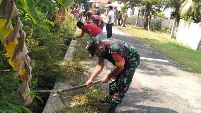Foto Babinsa Koramil 09/Telanaipura Sertu Erizal saat melaksanakan kerja bakti bersih-bersih rumput dan tumpukan sampah di saluran air di Jalan Sri Rezeki RT. 17, Kelurahan Beliung Kec. Alam Barajo, Kota Jambi.**